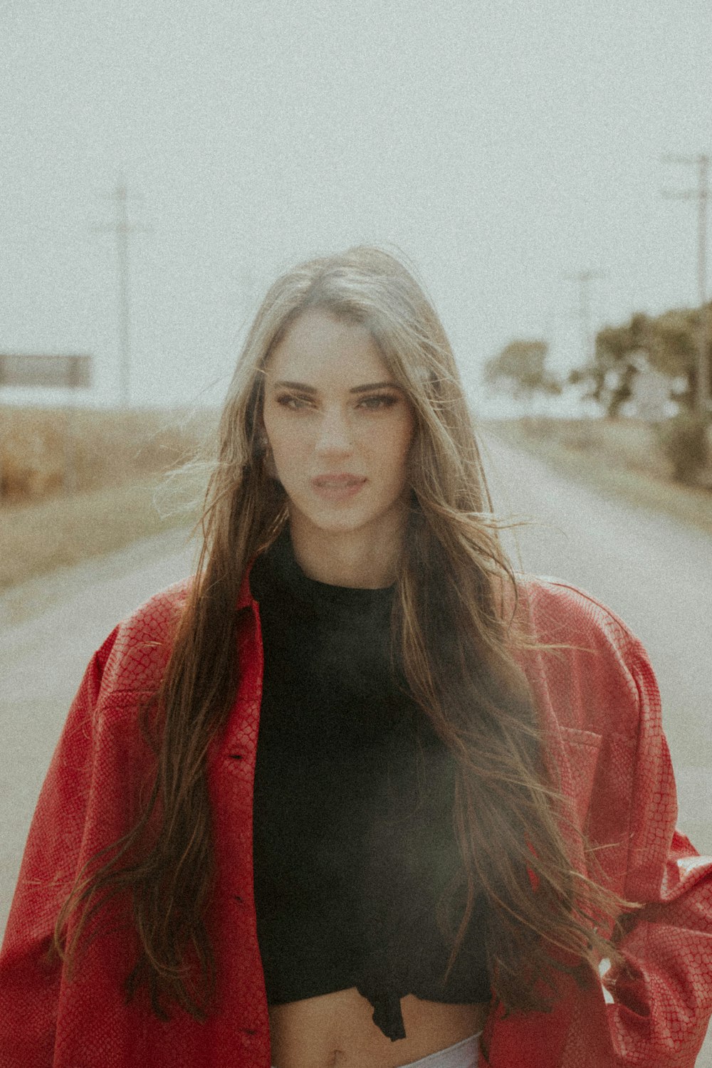 woman in black crew neck shirt and red jacket standing on road during daytime