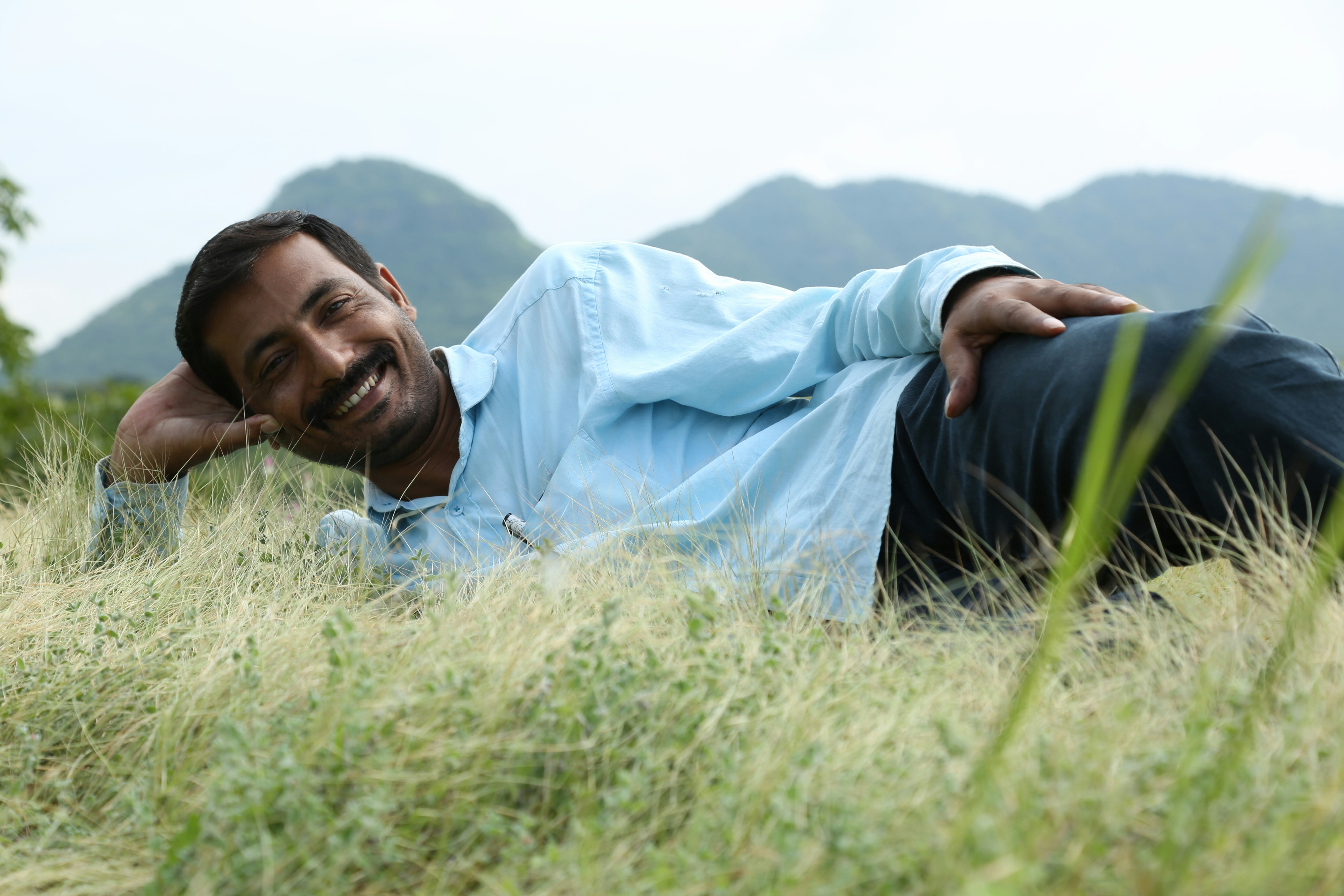man in blue dress shirt lying on green grass field during daytime