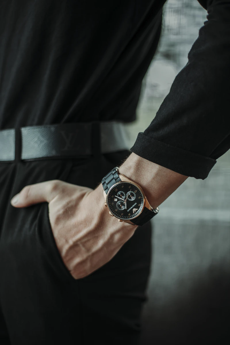 Man in dark clothing wearing a steel watch with his hand in his pocket