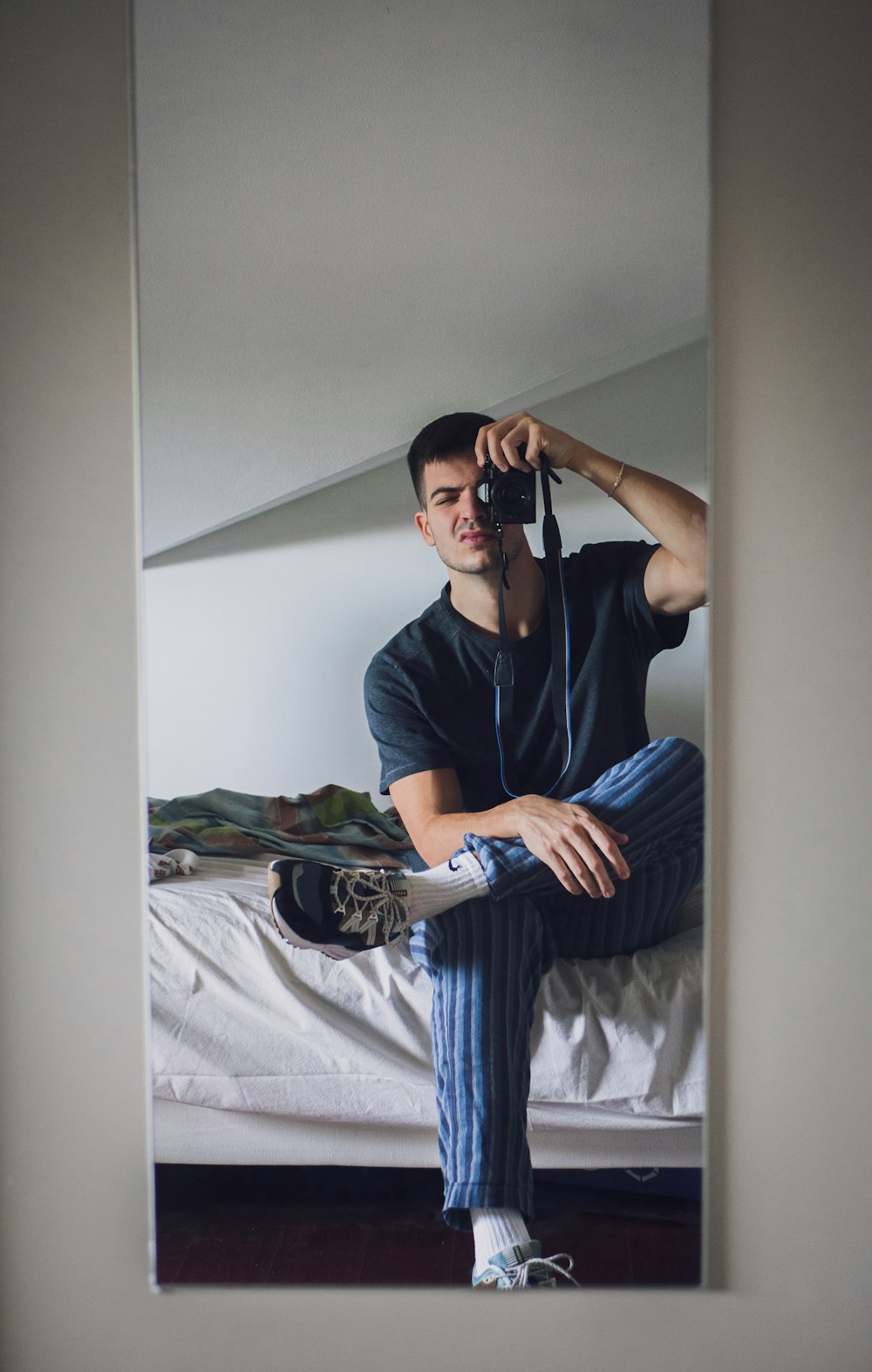 Hombre con camiseta negra de cuello redondo y pantalones azules sentado en la cama