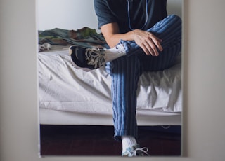 man in black crew neck t-shirt and blue pants sitting on bed