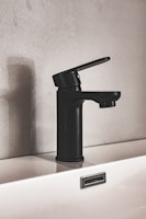 Minimalist wall-hung basin in matte black against a smooth grey wall with subtle lighting.
