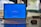 A laptop on a desk is displaying a blue screen with an update notification. The screen shows a progress indicator for Windows updates at 27%, along with text advising not to turn off the PC. A mouse is placed next to the laptop on the desk.
