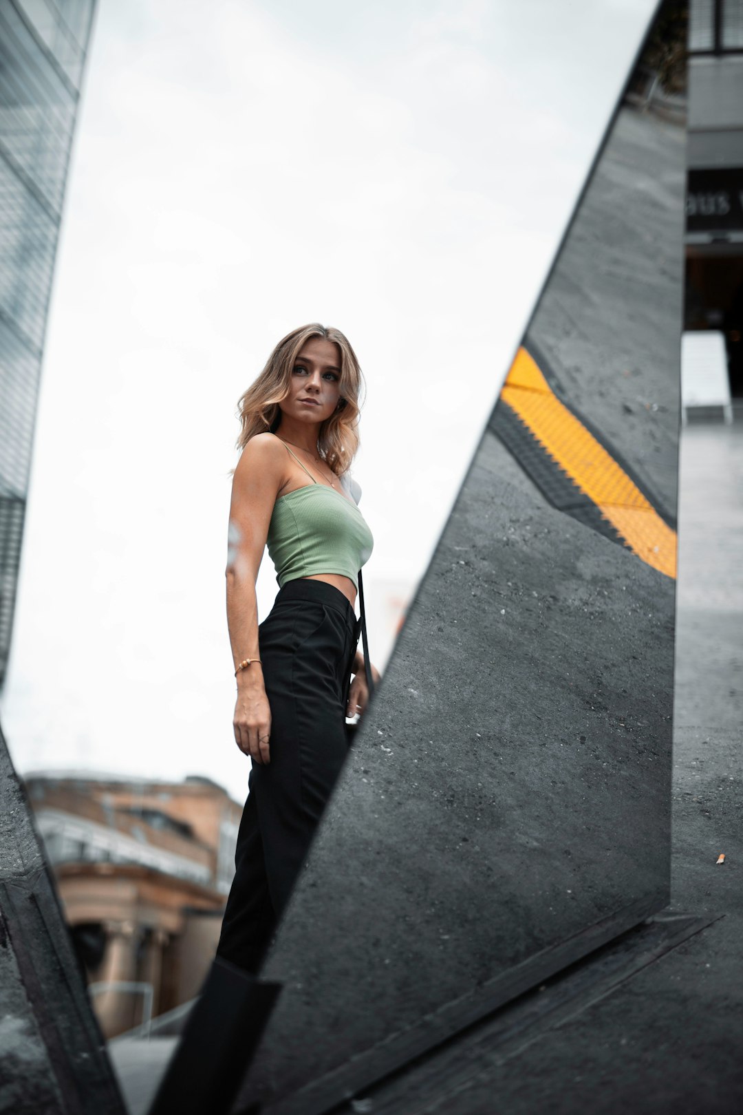 woman in green tank top and black pants standing on gray concrete floor