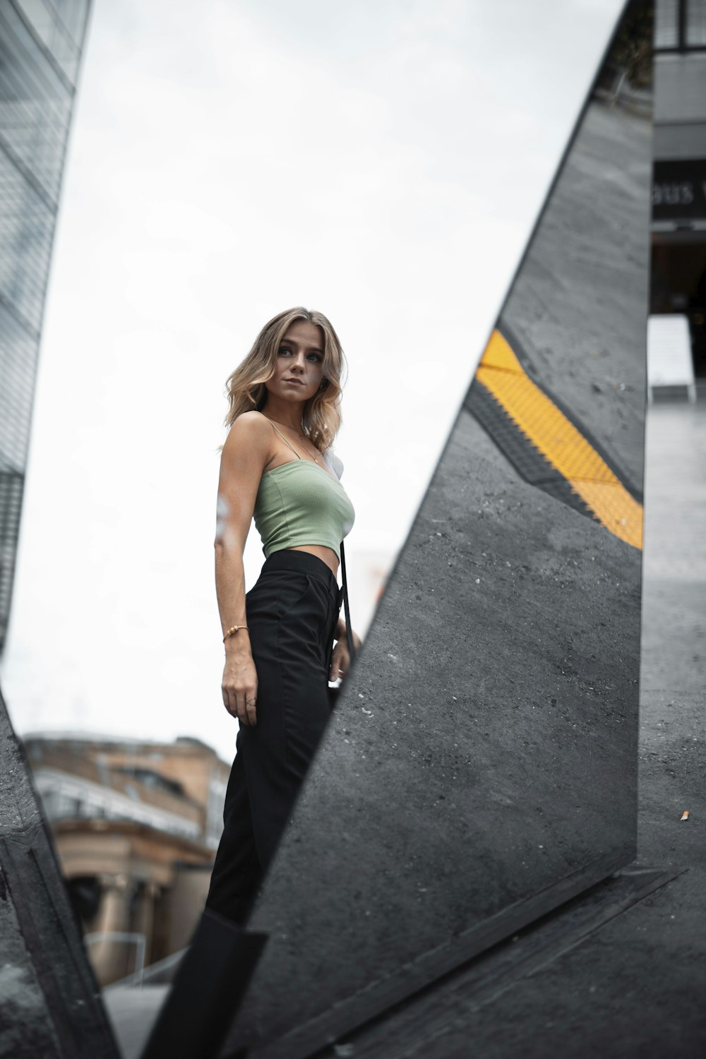 woman in green tank top and black pants standing on gray concrete floor