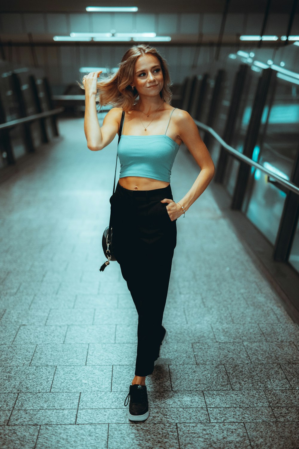 woman in blue spaghetti strap top and black pants standing on gray concrete floor