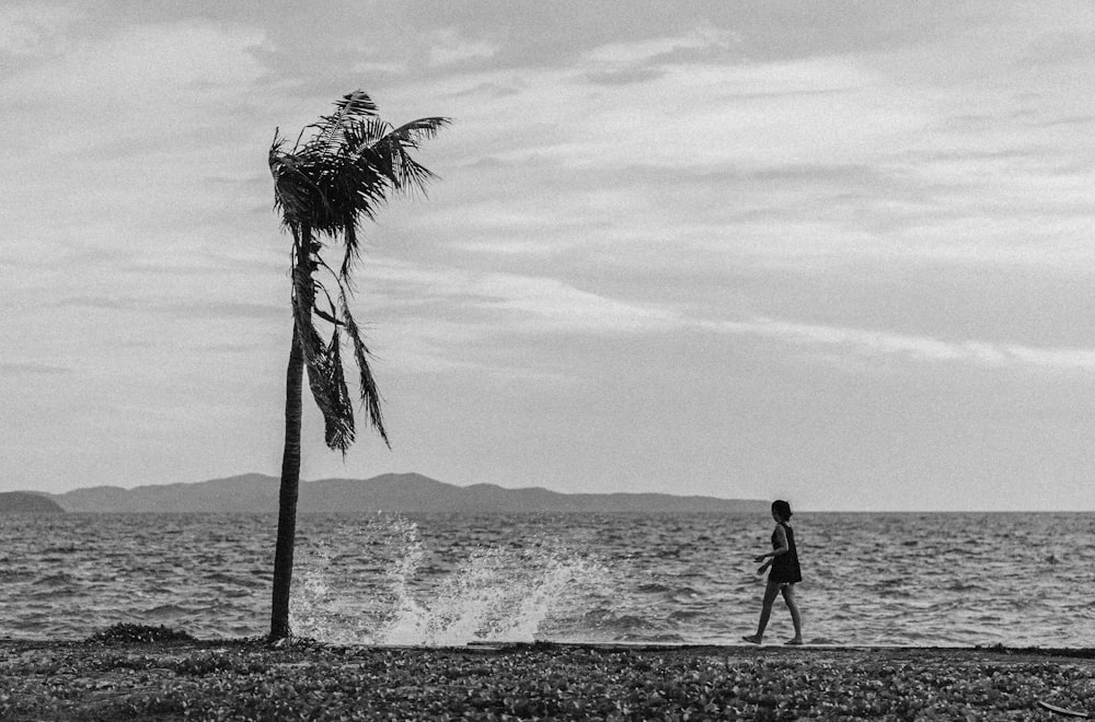 Graustufenfoto eines Mannes, der am Strand spazieren geht