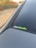 A close-up view of a car's rear window featuring a sticker with the text 'CarMeets'. The sticker has a combination of white and green lettering. The background is slightly blurred, with hints of greenery and a touch of autumn colors.