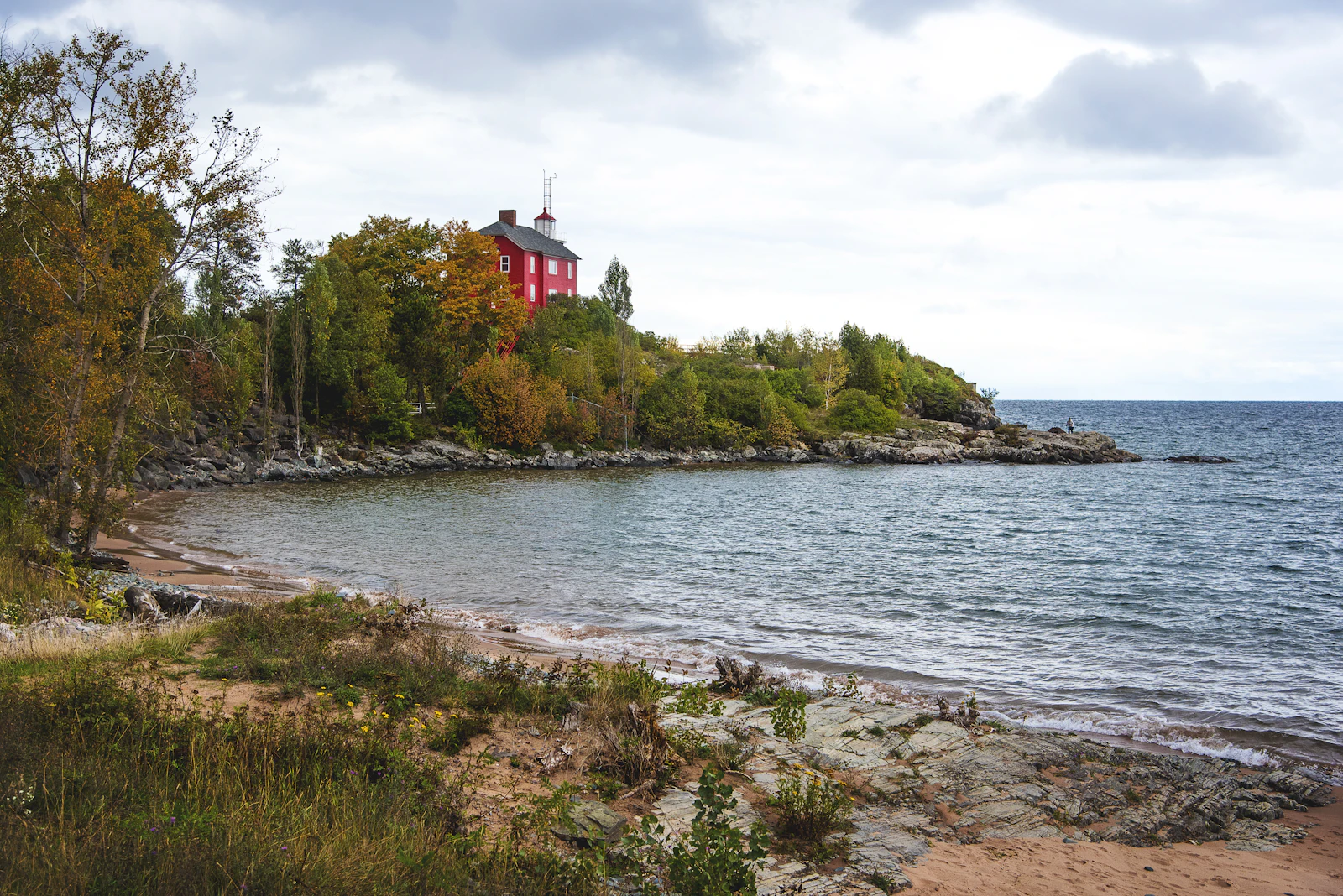 A wooded lakeshore with a red-roofed building at the point.