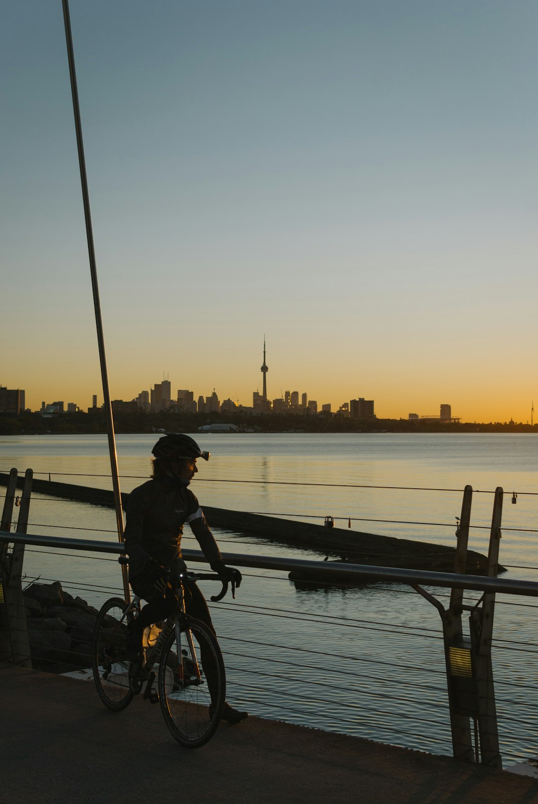 man in black jacket riding bicycle near body of water during sunset