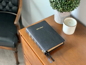 A softly lit candle beside an open Bible, symbolizing prayer and faith.