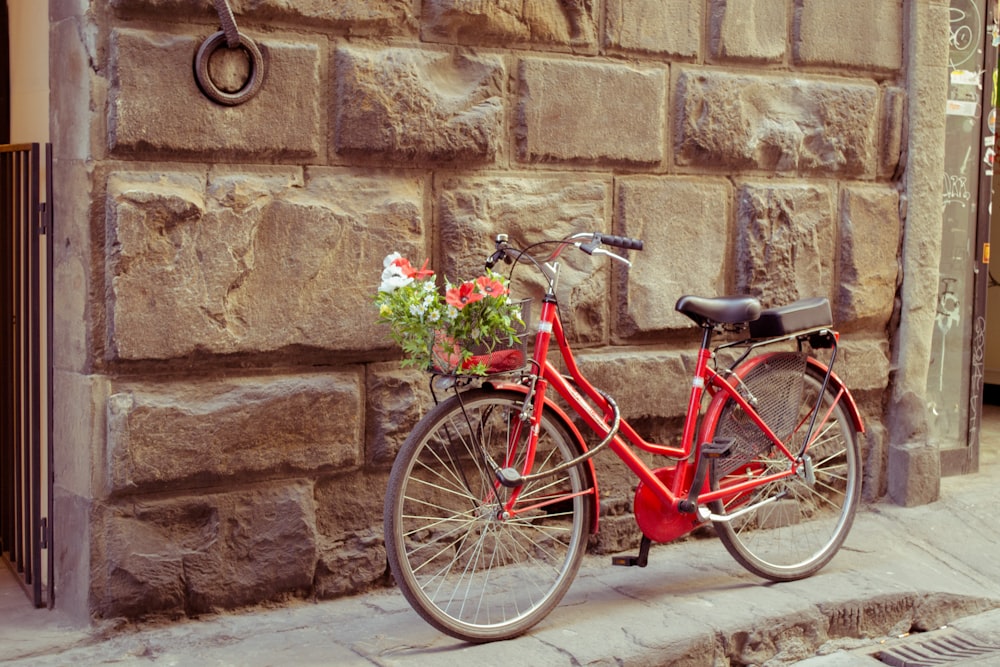 bicicleta vermelha estacionada ao lado da parede de tijolos marrons