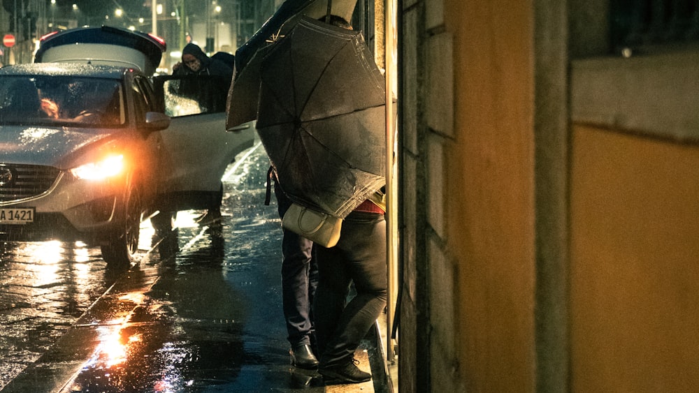 man in black jacket and blue denim jeans holding umbrella walking on sidewalk during daytime