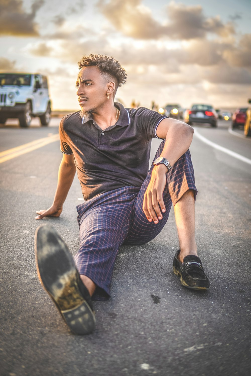 man in black crew neck t-shirt and blue and white plaid pants sitting on road