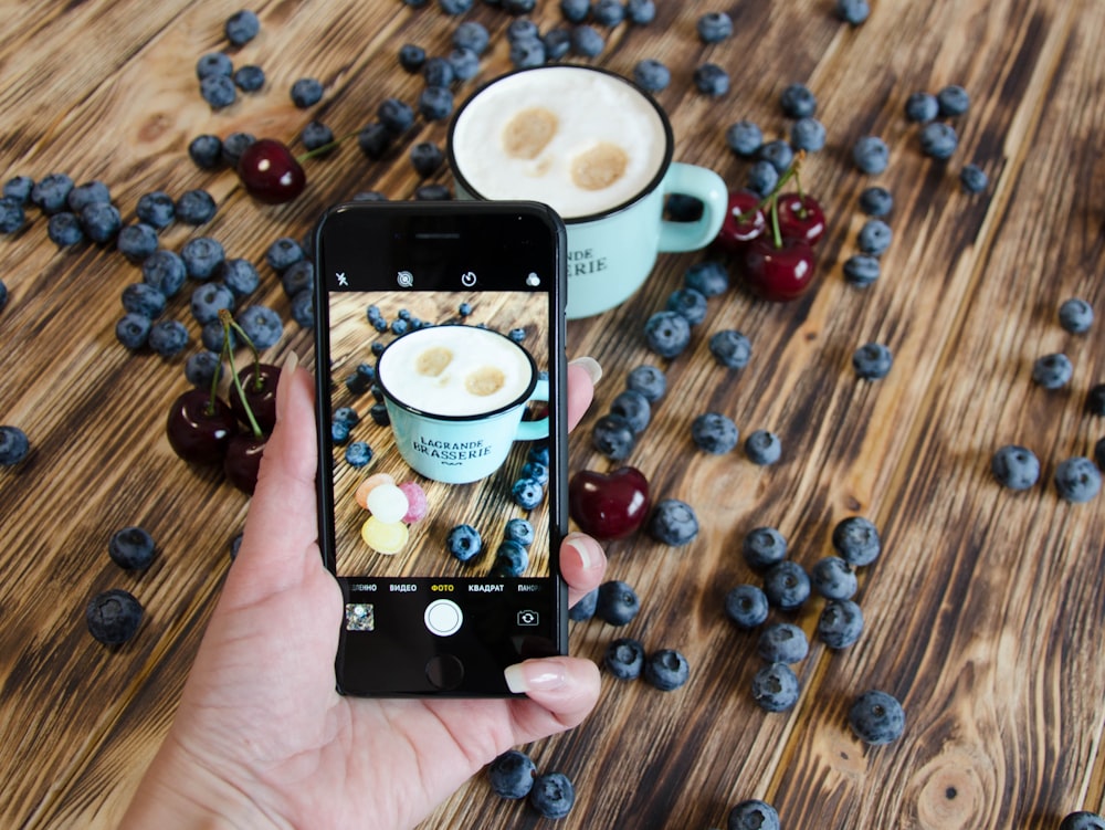 person holding black iphone 4 taking photo of coffee beans on brown wooden table