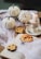 A cozy Halloween scene featuring white pumpkins, spider decorations, and cookies in the shape of skulls and a jack-o'-lantern. The setup includes a burning candle placed on a saucer with cobweb-like material scattered across an open book.