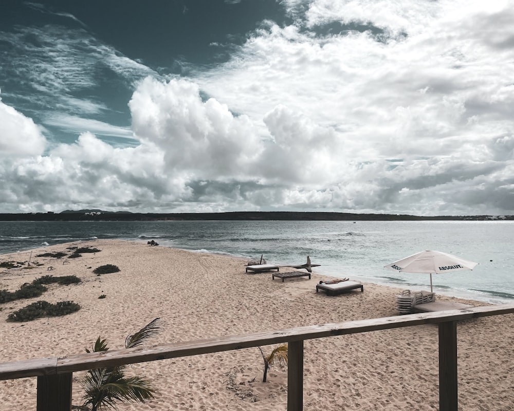 white and black beach lounge chairs on beach shore under blue and white sunny cloudy sky