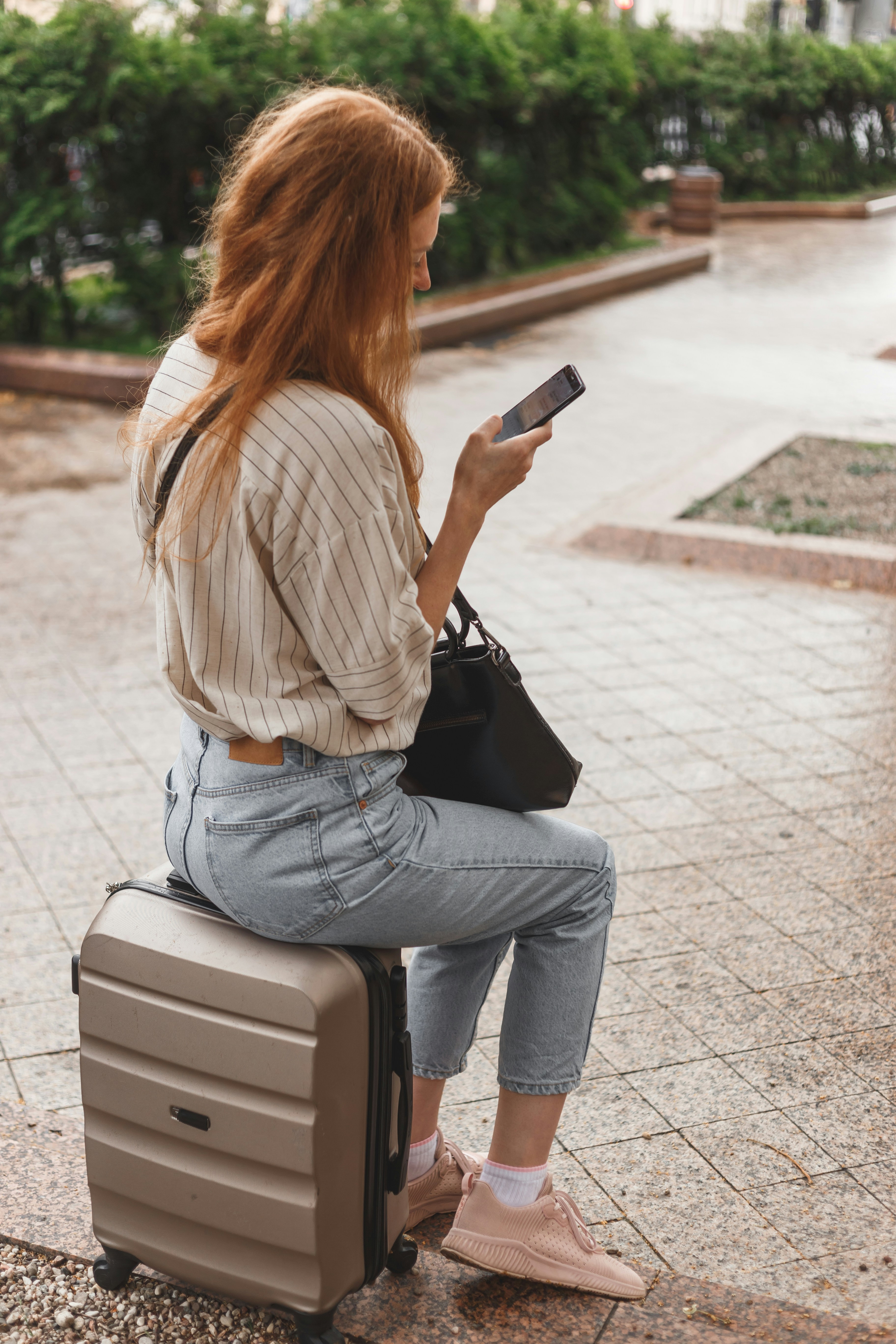 woman in white long sleeve shirt and blue denim jeans sitting on white and black luggage