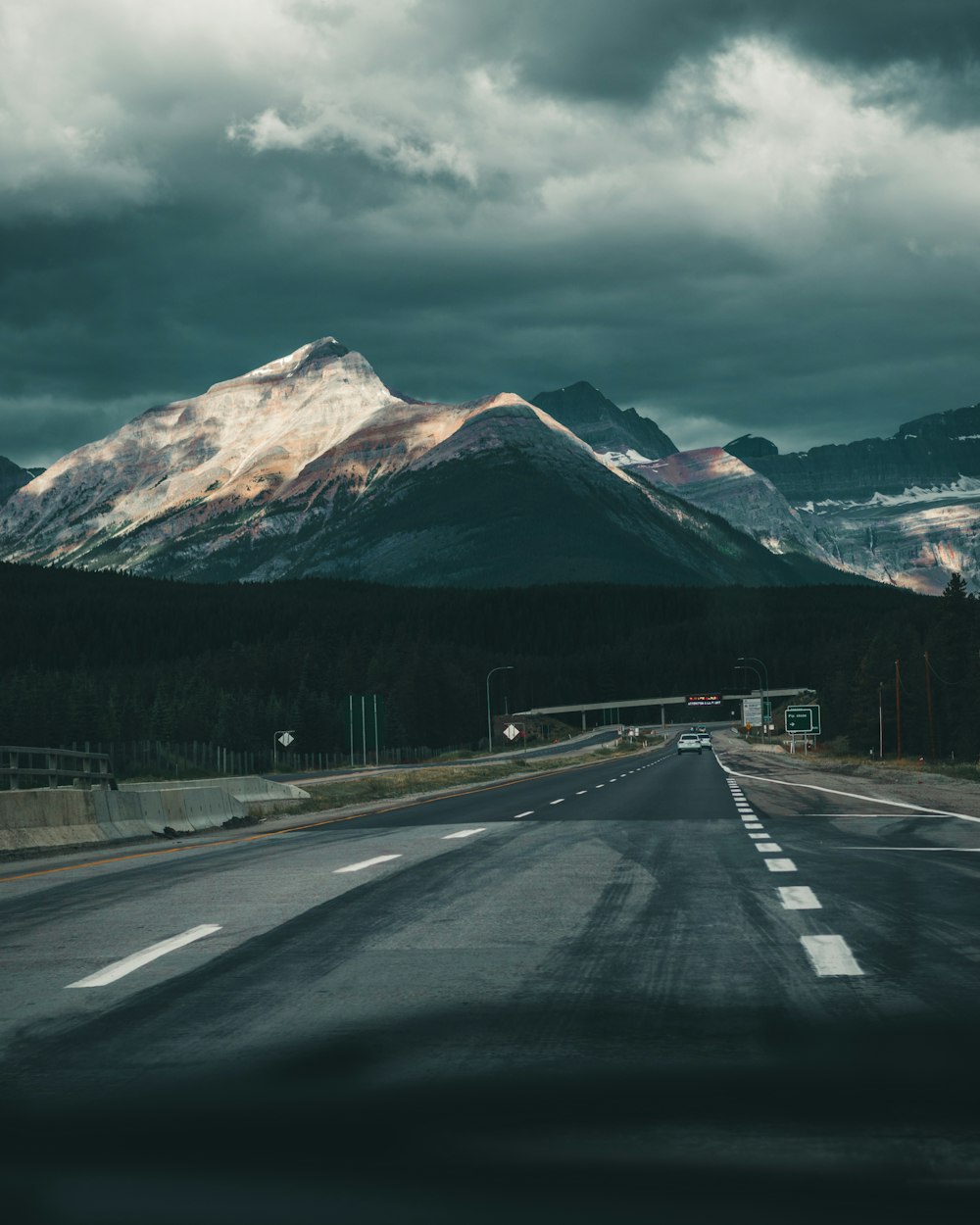 gray asphalt road near mountain under cloudy sky during daytime