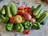 An assortment of fresh vegetables including cucumbers, red tomatoes, green bell peppers, and onions are arranged together on a patterned surface. The vegetables display a variety of shapes and vibrant colors, indicating freshness and abundance.