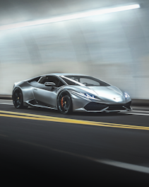 A sleek, silver sports car speeding through a tunnel. The streamlined design is accentuated by the bright tunnel lights reflecting off its metallic surface, creating a sense of movement and dynamism.