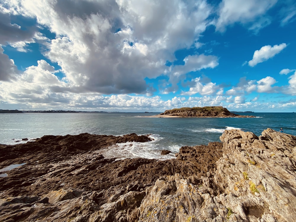 brown rock formation near body of water under blue and white cloudy sky during daytime