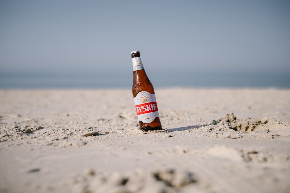 brown and white labeled bottle on white sand during daytime