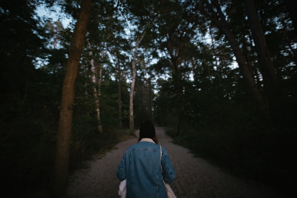 man in blue hoodie walking on pathway in between trees during daytime