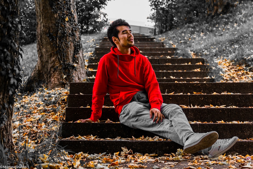 man in red hoodie sitting on brown concrete stairs