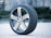 A single car tire with a detailed tread pattern is positioned upright on a brick pavement. The tire features a shiny alloy wheel with a Volkswagen logo in the center. The background is slightly blurred, highlighting the tire as the main focus.