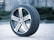 A single car tire with a detailed tread pattern is positioned upright on a brick pavement. The tire features a shiny alloy wheel with a Volkswagen logo in the center. The background is slightly blurred, highlighting the tire as the main focus.