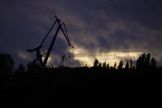 A powerful shot of a massive H-beam being lifted by a crane against a dark sky.