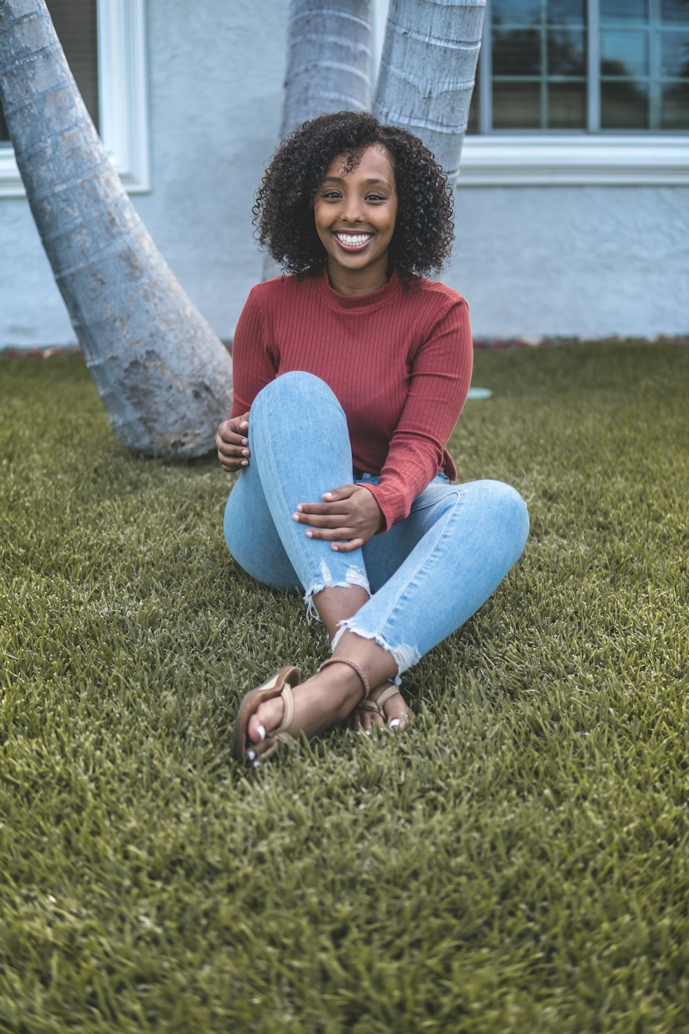 woman in red sweater and blue denim jeans sitting on green grass field during daytime