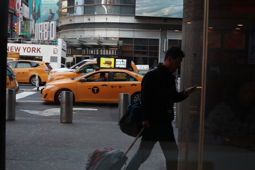 man in black jacket and black pants holding stick near yellow taxi cab