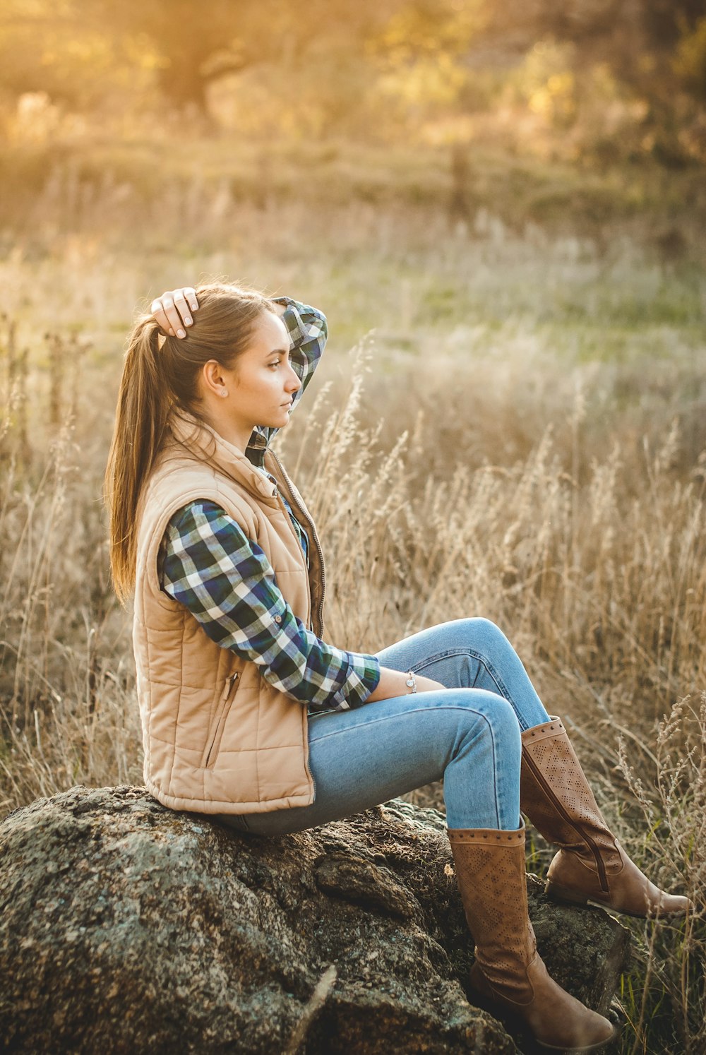 woman in blue and white plaid dress shirt and blue denim jeans sitting on rock during