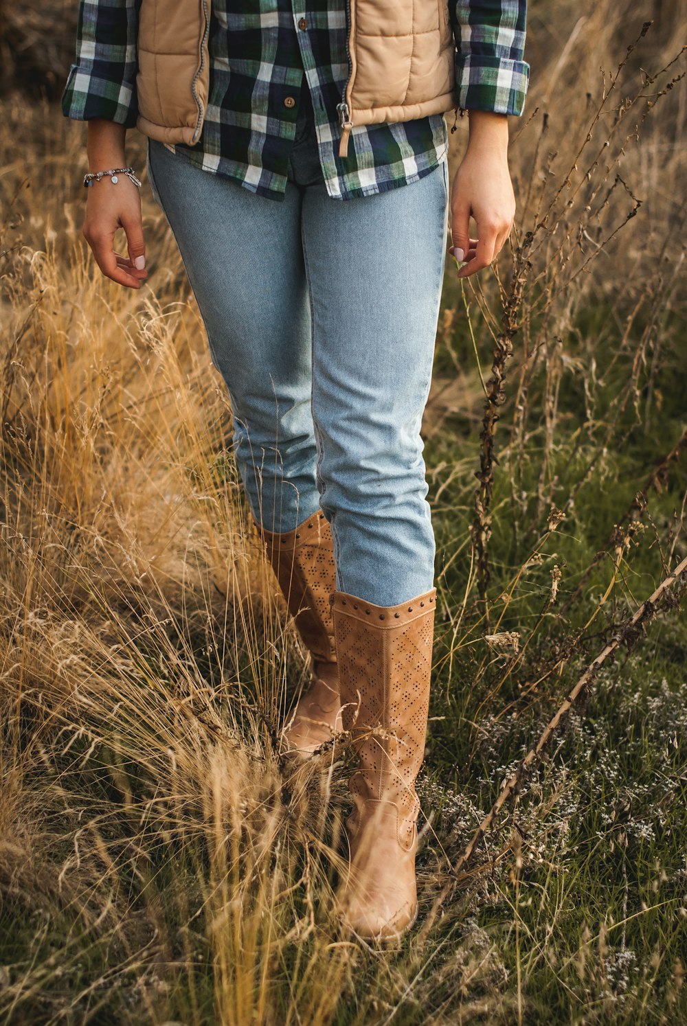 pessoa em jeans azuis e botas marrons em pé no campo de grama verde durante o dia