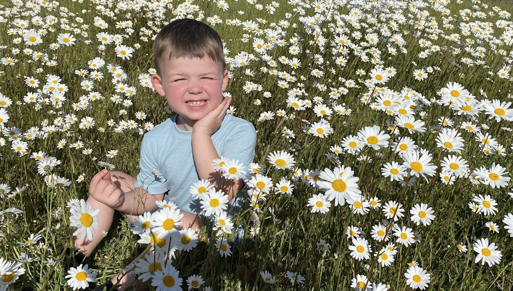 boy in blue crew neck t-shirt sitting on yellow flower field during daytime
