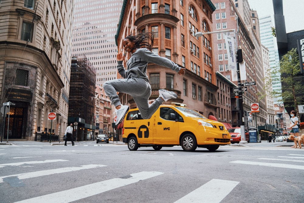 man in black jacket and gray pants jumping on yellow cab