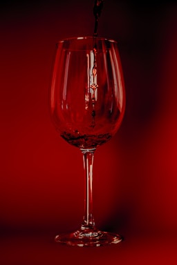 A close-up of a wine glass being filled with deep red wine