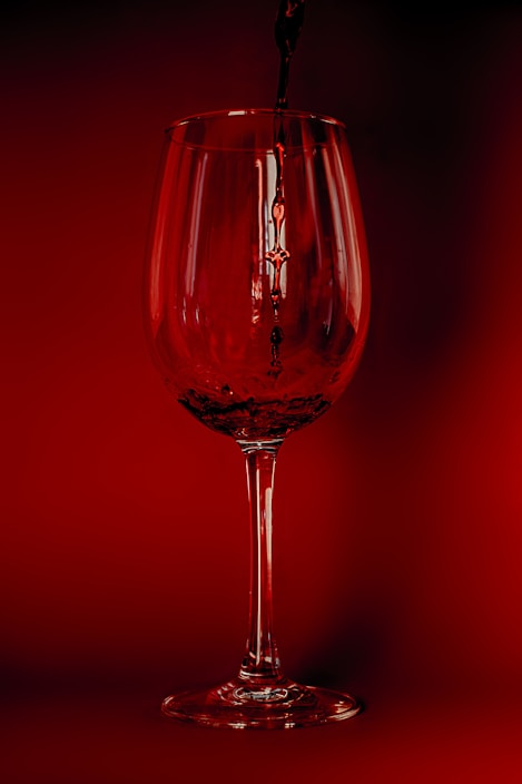 A close-up of a wine glass being filled with deep red wine
