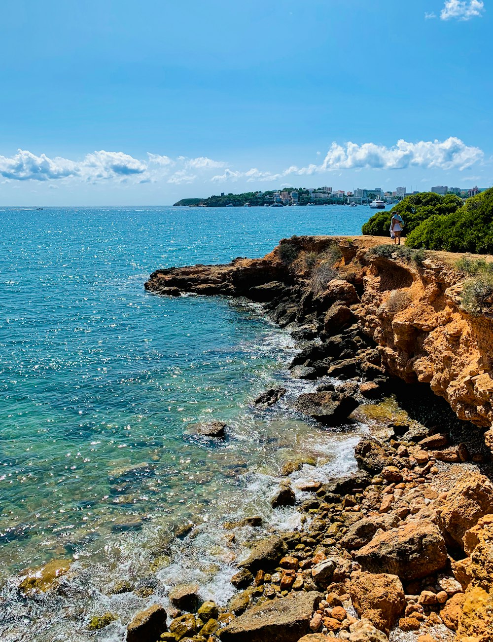 brown rocky mountain beside blue sea under blue sky during daytime