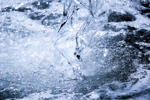 A dynamic capture of water in motion, featuring splashes and foam with intricate textures and bubbles. The scene is dominated by various shades of blue and white, emphasizing the fluidity and movement of the water.