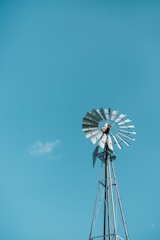 A tall windmill spinning steadily against a clear blue sky at an industrial site.
