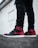 A pair of stylish sneakers with black and red coloring worn with ripped black jeans. The setting appears urban, with a white wall in the background.