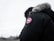 A person is wearing a dark parka with a fur-lined hood and a distinct round patch featuring a logo on the sleeve. The background is a cloudy, overcast sky, and the focus is on the jacket.