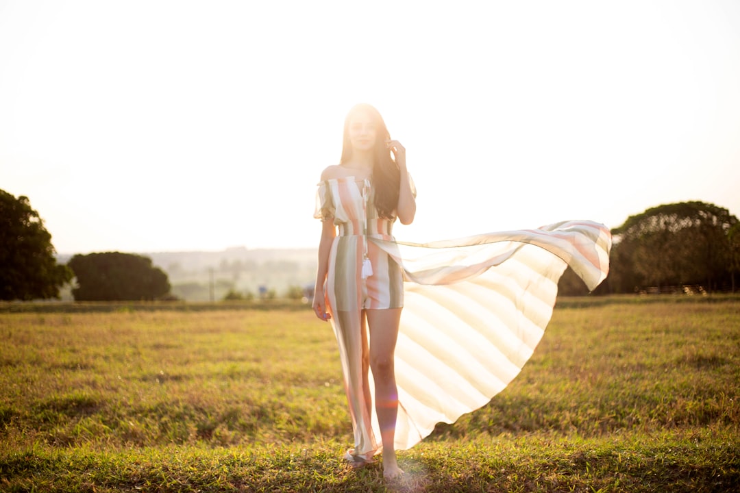 woman in white and brown striped dress standing on green grass field during daytime