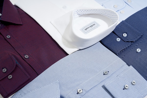 Several neatly arranged dress shirts featuring various patterns and colors, including white, burgundy, dark blue, and light blue. The shirts display button details and fine fabric textures, reflecting a sense of organization and style.