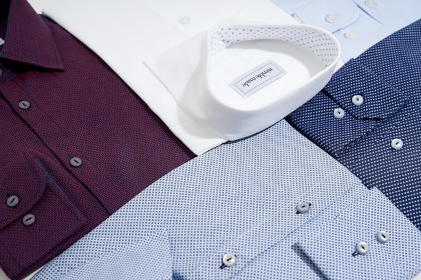Several neatly arranged dress shirts featuring various patterns and colors, including white, burgundy, dark blue, and light blue. The shirts display button details and fine fabric textures, reflecting a sense of organization and style.