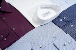 Several neatly arranged dress shirts featuring various patterns and colors, including white, burgundy, dark blue, and light blue. The shirts display button details and fine fabric textures, reflecting a sense of organization and style.