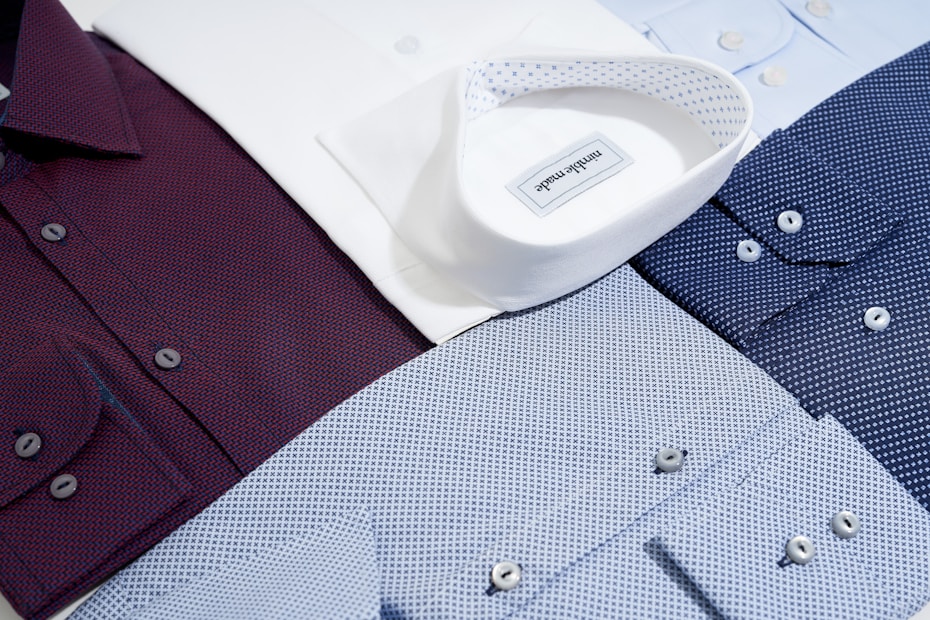 Several neatly arranged dress shirts featuring various patterns and colors, including white, burgundy, dark blue, and light blue. The shirts display button details and fine fabric textures, reflecting a sense of organization and style.